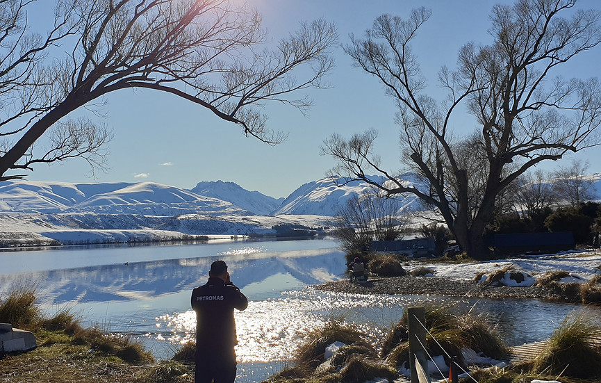 Jeff Ng taking photos at Lake Alexandrina with snow capped mountains in the background and sun sparkling on the water