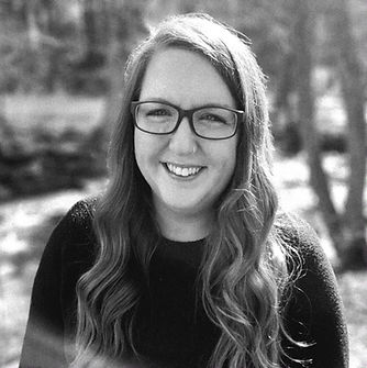 Photo of Maggie with glasses, long hair, smiling.