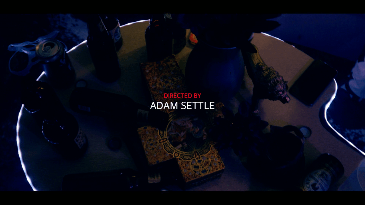 directed by adam settle credit appears over cinematic shot of a table with beer bottles flowers and a cross under colored lighting