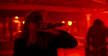 Heaavy metal band performs in a dark grungy warehouse under red saturated lighting in horror makeup