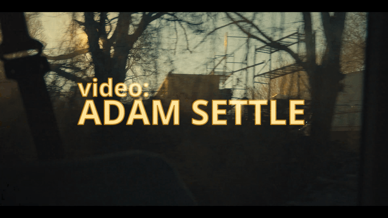 video: Adam Settle credit superimposed over a sunset shot through a moving vehicle window of construction area
