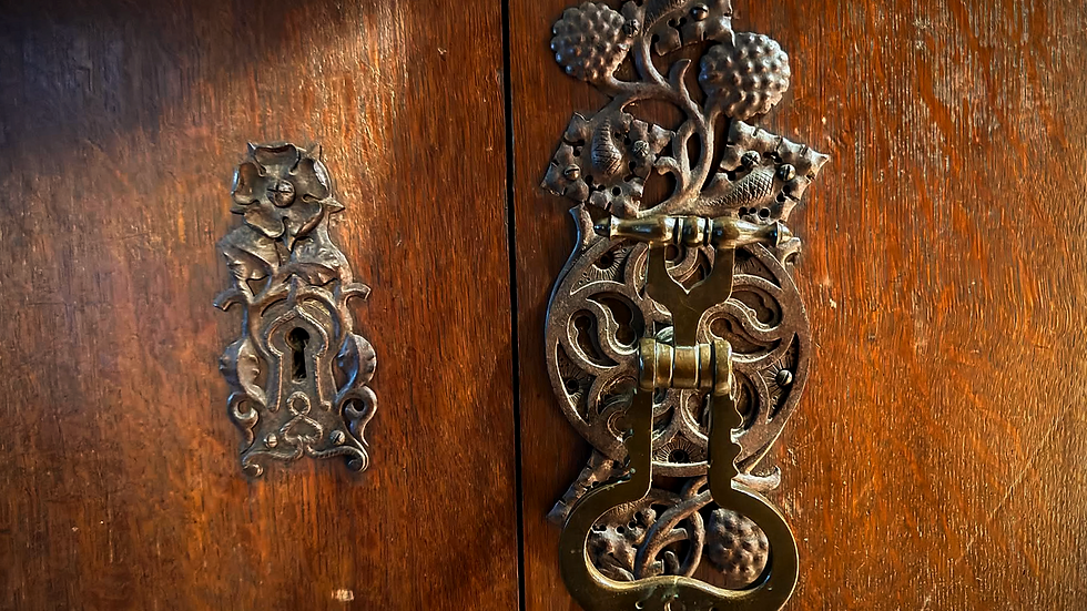 A wooden door with a metalwork lock and handle. Twined around the lock is a rose, also in metalwork. The handle is similarly decorated with twining foliage.