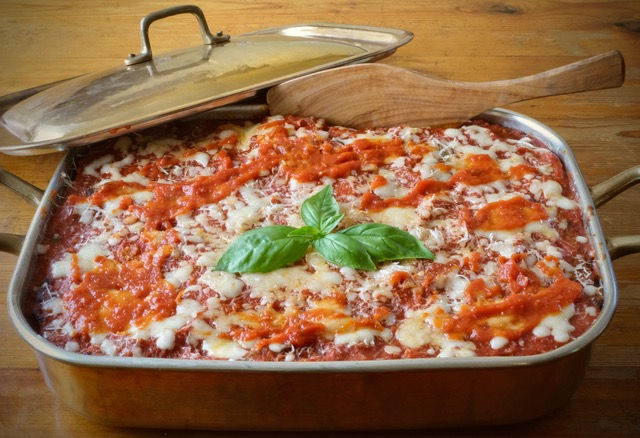 Eggplant parmesan in copper dish with wooden spoon and sprig of basil