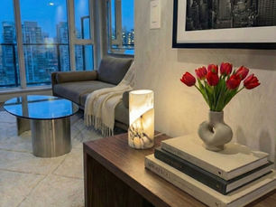 Entryway to a high-rise luxury apartment. The hand crafted Carrara marble lamp provides a soft glow as dusk. On the table a few books with a vase and red tulips. Over the wood table a modern black and white cityscape photo hangs