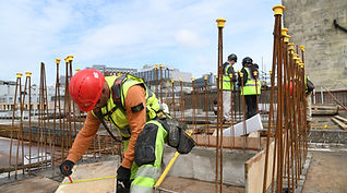 Site worker kneeling and taking measurements on a reinforced concrete rebar structure.