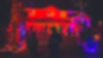Halloween scene with people in costumes, glowing red-lit house, and vivid decorations like skeletons and pumpkins. Eerie and festive vibe.