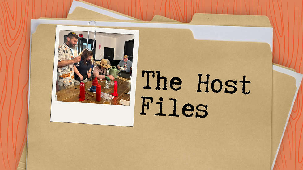 Group cooking in a bright room, focused on condiments. One person wears a hat. Background includes wooden texture and file folders labeled "The Host Files".