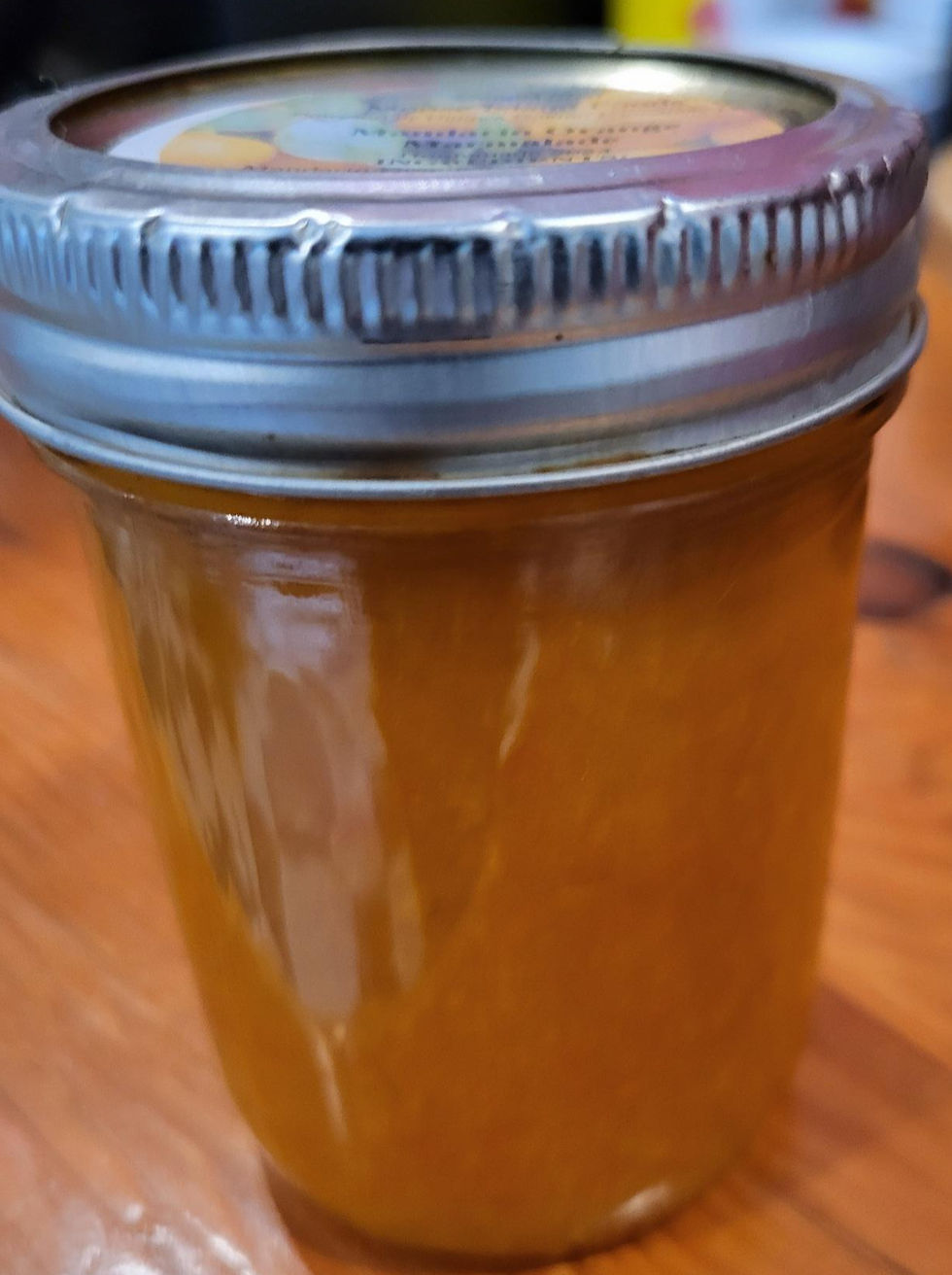 Miniaturbild: This image showcases a glass jar filled with an orange preserve, possibly jam or marmalade. The jar features a metal lid and is placed on a rustic wooden surface, adding charm to its presentation.