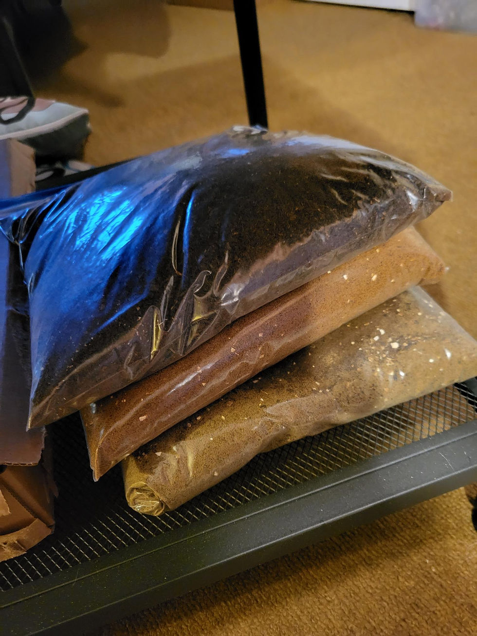 Stacked plastic bags of potting soil on a black mesh shelf indoors, with warm tan carpet and a blue reflection on the top bag