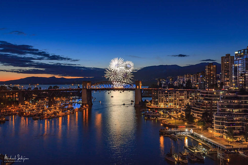 Fireworks light up the night sky above Vancouver's Burrard Bridge, set against the breathtaking backdrop of the city's sparkling skyline.
