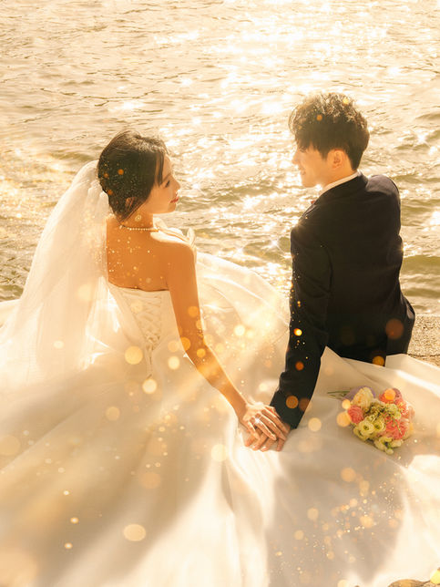 Couple de mariés assis au bord de l'eau au coucher du soleil, photographie de mariage romantique en extérieur.