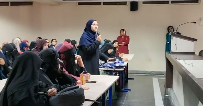 Woman speaking into microphone at a seminar with audience members.