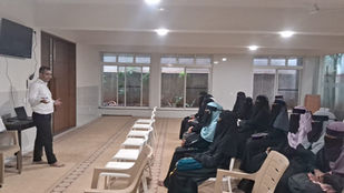 Man presenting to an audience of veiled women in a large room.