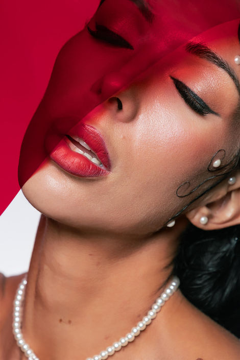 Moody, high-fashion editorial close-up showing vibrant red lipstick and artistic face pearls under creative red lighting