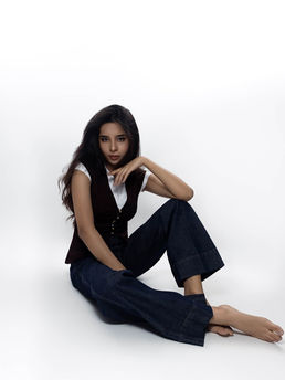 Female posing for fashion editorial modelling portrait with jeans and a vest sitting on the studio floor