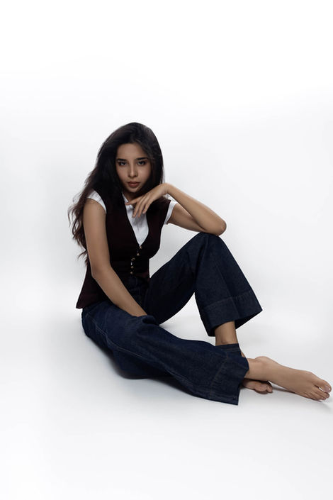Female posing for fashion editorial modelling portrait with jeans and a vest sitting on the studio floor