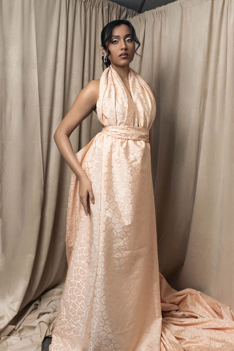 Fashion portrait of a model in a peach-hued silk gown featuring a metallic geometric pattern and expert fabric draping, captured in a luxury photography studio.