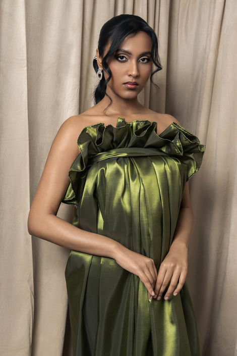 Cinematic fashion portrait featuring a woman in a rich moss-green silk dress with a ruffled neckline, highlighting soft lighting and luxury editorial styling for a high-end brand.
