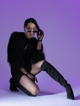 Toronto editorial photography: Model wearing clear sunglasses and a black shaggy coat, kneeling on a purple set.