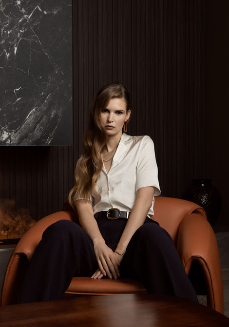 Woman with arms crossed sitting in orange chair with white top and blue pants