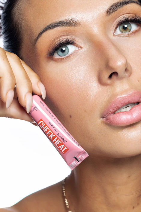 Macro beauty portrait of a model holding Maybelline Cheek Heat blush, showcasing detailed skin texture and professional product photography.