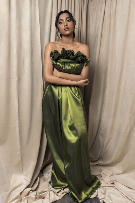 Minimalist fine art portrait of a model in a draped olive green satin gown with arms crossed, showcasing elegant composition and high-end studio photography techniques.
