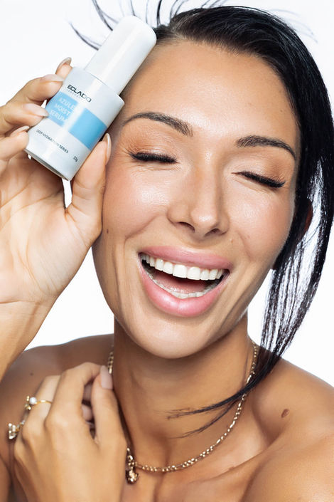 A smiling model holding the Eclado Azulene Moist Serum, captured with bright, commercial lighting for a beauty product feature