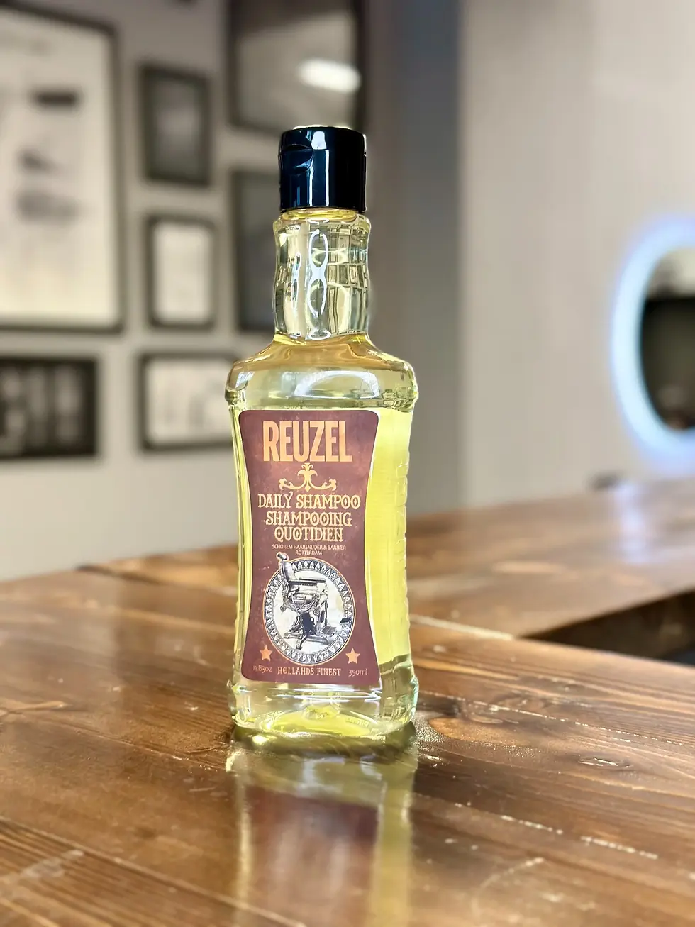 Reuzel Daily Shampoo na dřevěném pultu v barbershopu The Looks, ideální pro každodenní péči o vlasy.