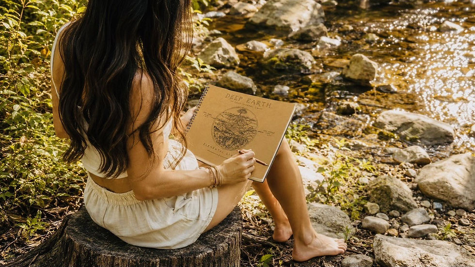Woman writing in her art journal while sitting on a creek bank.