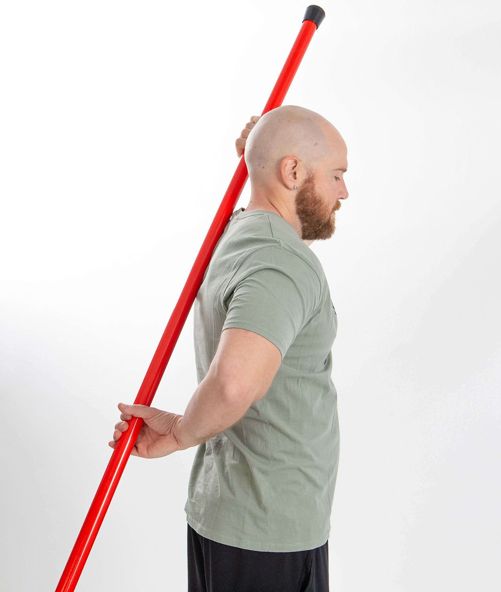 Mike is demonstrating a shoulder mobility stretch using a red exercise stick held vertically behind his back, with one hand reaching overhead and the other behind his lower back.