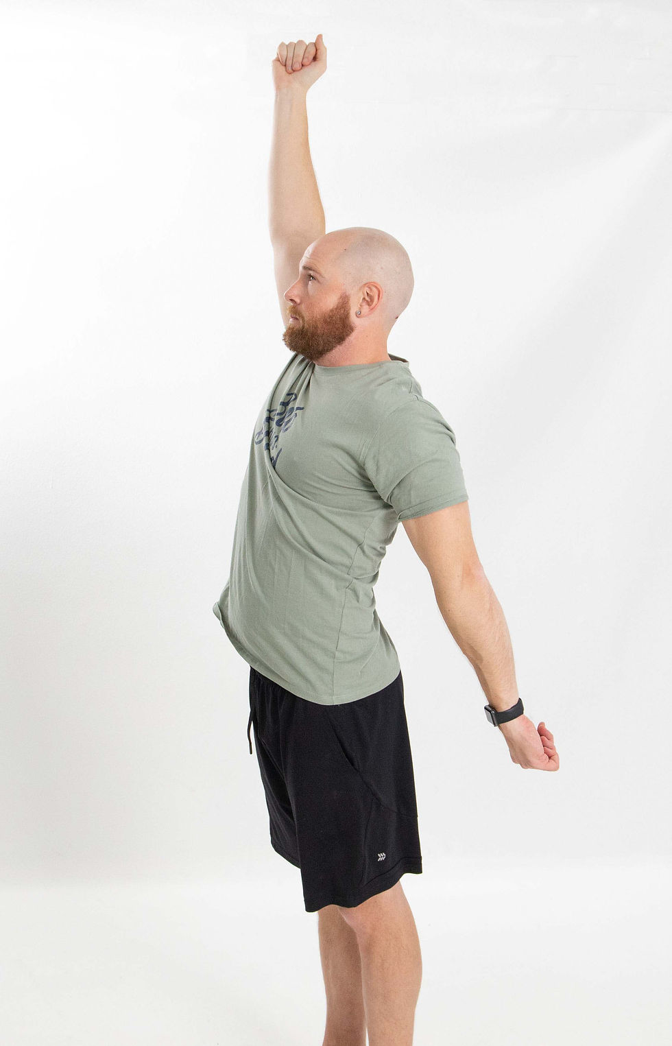 Side view of a man standing with his chest lifted and back slightly arched, extending one arm overhead and the other behind his body to stretch his chest, shoulders, and upper back.