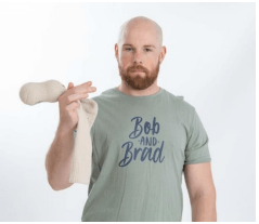 Mike wearing a green Bob and Brad T-shirt, holding a white sock with 2 lacrosse balls over his right shoulder against a plain white background.