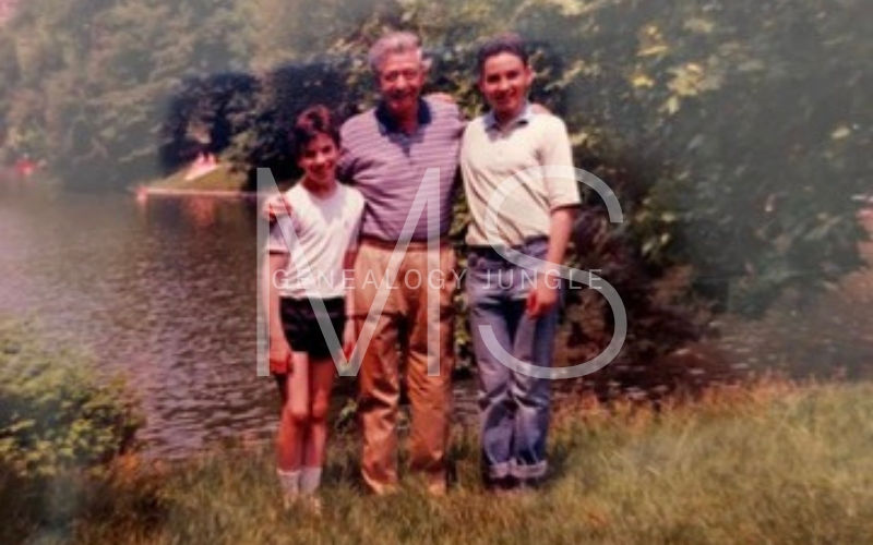 Three people pose by a lake in a park, smiling. They're wearing casual clothes. The background has trees and greenery, creating a warm mood.