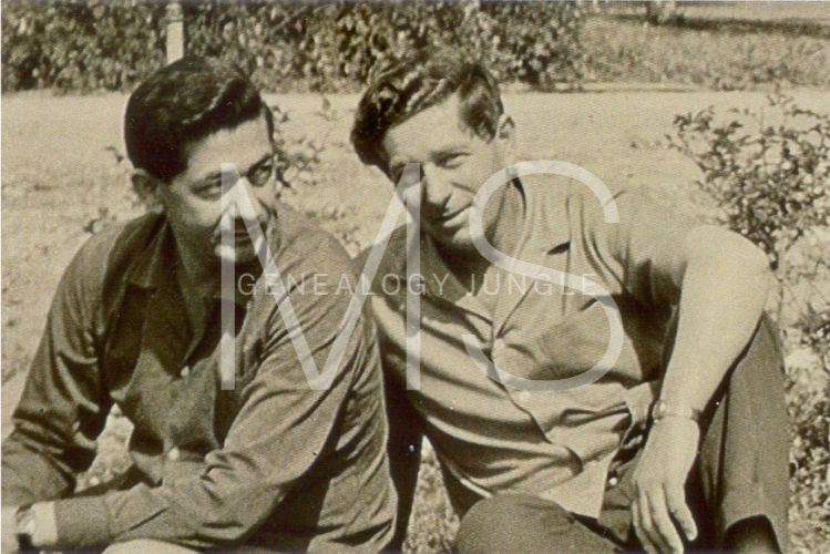 Two men sit closely in a garden, both smiling and wearing casual dark shirts. The mood is relaxed and friendly. Large text overlays the image.