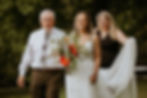 Bride walking down the aisle with her father and her wedding coordinator holding her dress