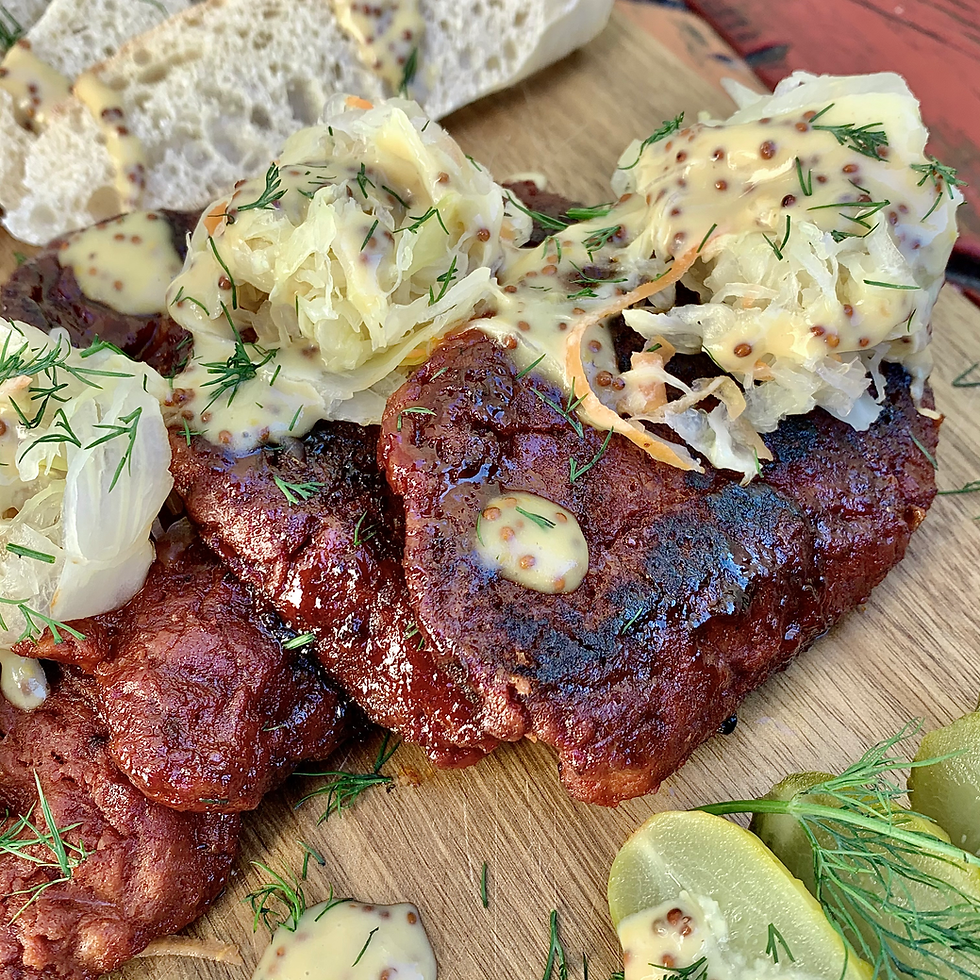 Close-up of whole-food plant-based steaks topped with sauerkraut and creamy dill sauce, served with bread and fresh lime on a wooden board.