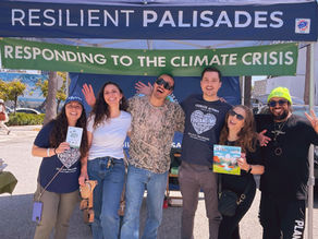 The Vegan Solutions Team stand together smiling in front of a Resilient Palisades canopy that reads “Responding to the Climate Crisis.” They have their arms around each other, and one person holds a vegan children's book. The group is outdoors in daylight with trees and street in the background.