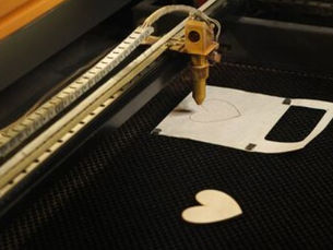 Cabezal láser sobre un panel de madera y una pieza con forma de corazón