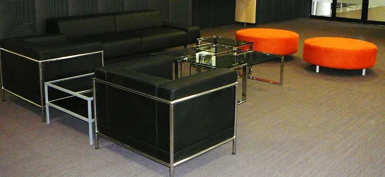 Modern lounge space with black sofas, glass table, orange ottomans