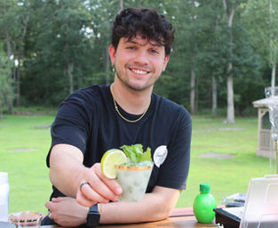 Michael Mellor, co-owner of Sunshine Sips Mobile Bar, smiling while serving a mint lime mocktail at an outdoor event.