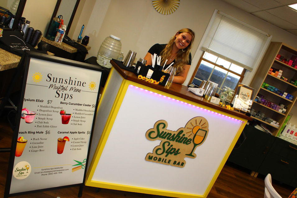 Sunshine Sips bartender smiling behind mobile mocktail bar at Elysium Hair Artistry Grand Opening in Wenonah, NJ.