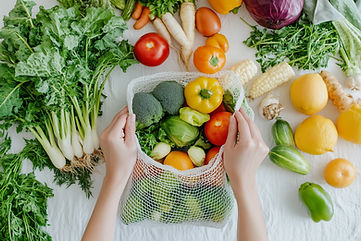 Close-up of hands placing fresh vegetables and fruits into an eco-mesh bag on a white tabl