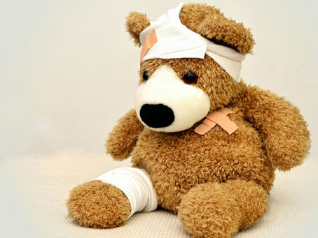 A well-loved teddy bear sits with bandages wrapped around its head and leg, recovering from an imaginary adventure.