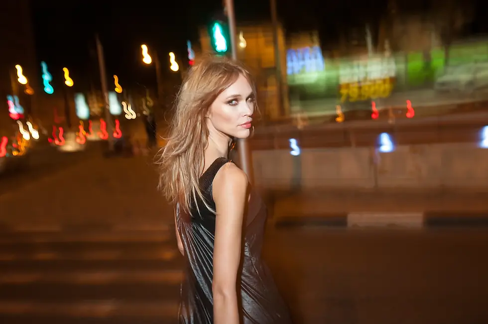 צילום אופנה לילי של דוגמנית בלבוש עור שחור על רקע אורות עיר מטושטשים ומריחת תנועה אורבנית
