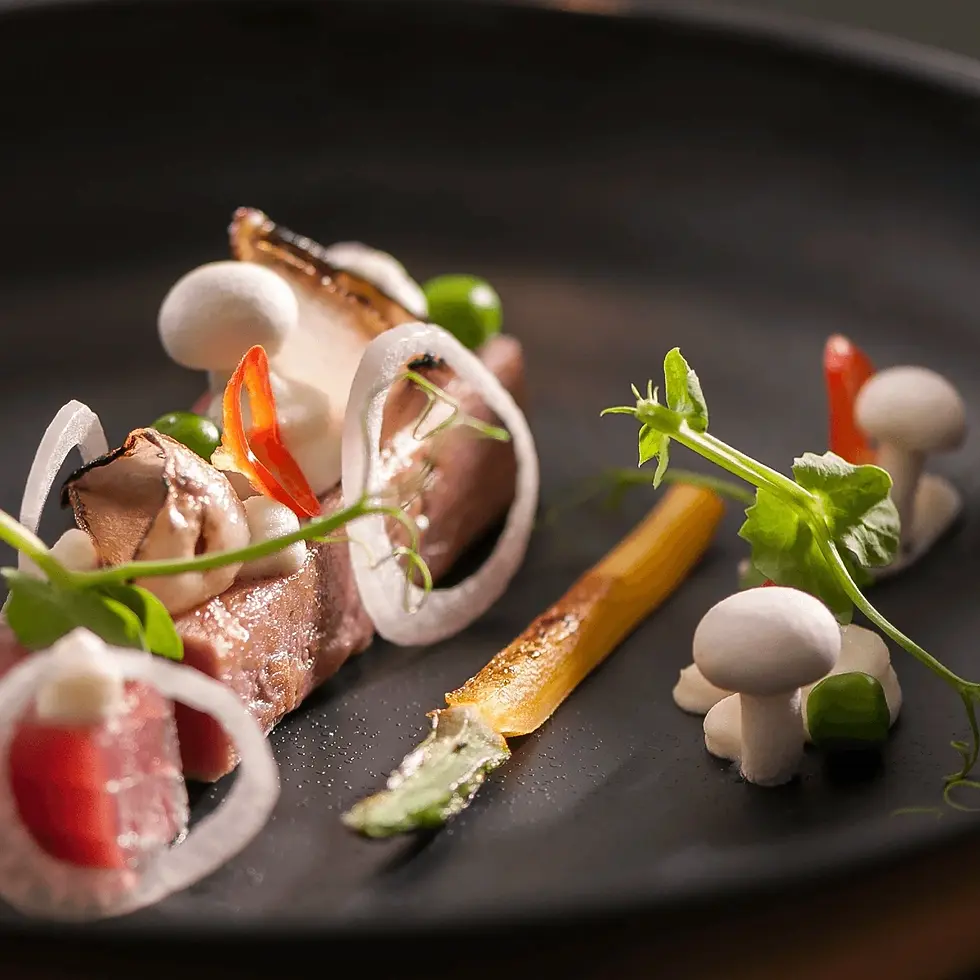 צילום מנת גורמה מוקפדת של נתחי דג נא עם ירקות מיקרו, פטריות ובצל על צלחת שחורה