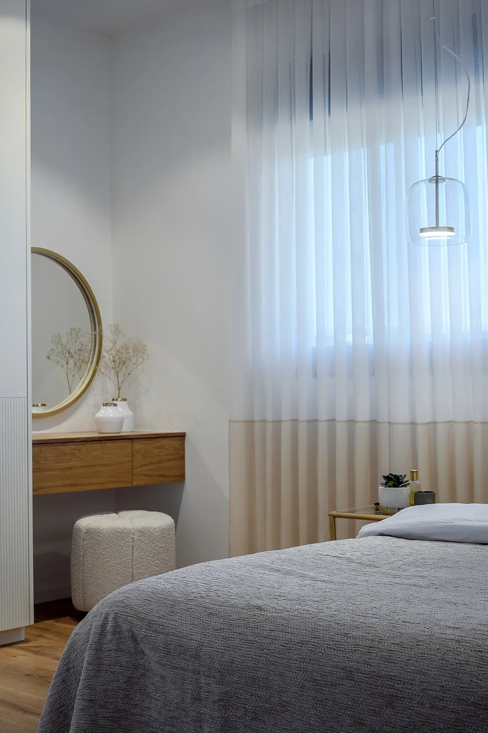 פינת התארגנות בחדר שינה הכוללת שולחן עץ צף, מראה עגולה, פוף מעוצב ותאורה רכה מבעד לוילון לבן