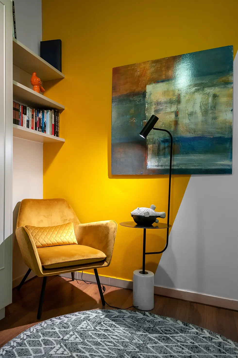פינת קריאה מעוצבת עם קיר צהוב, כורסת קטיפה בצבע חרדל, ציור מופשט ומנורת עמידה מודרנית