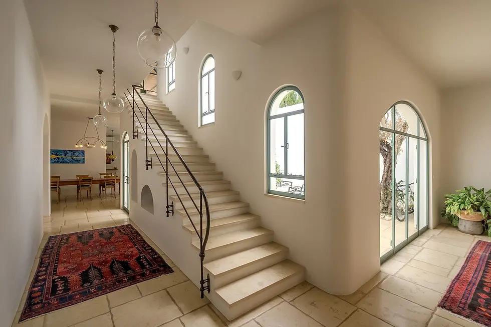 מסדרון פנים לבן ויוקרתי עם חלונות קשת, ריצוף אבן טבעית ומדרגות עם מעקה ברזל נפחות
