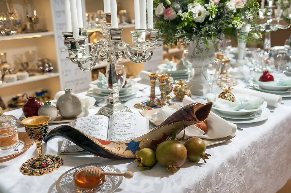 שולחן ערוך וחגיגי עם פריטי יודאיקה הכוללים שופר מעוטר, פמוטי כסף, רימונים ודבש