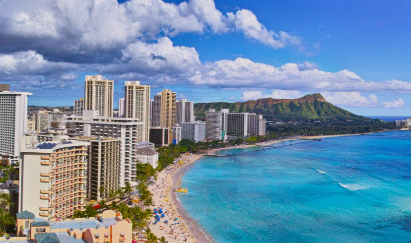Waikiki Beach with high-rise hotels, crowded shoreline, turquoise ocean, and Diamond Head under bright clouds.